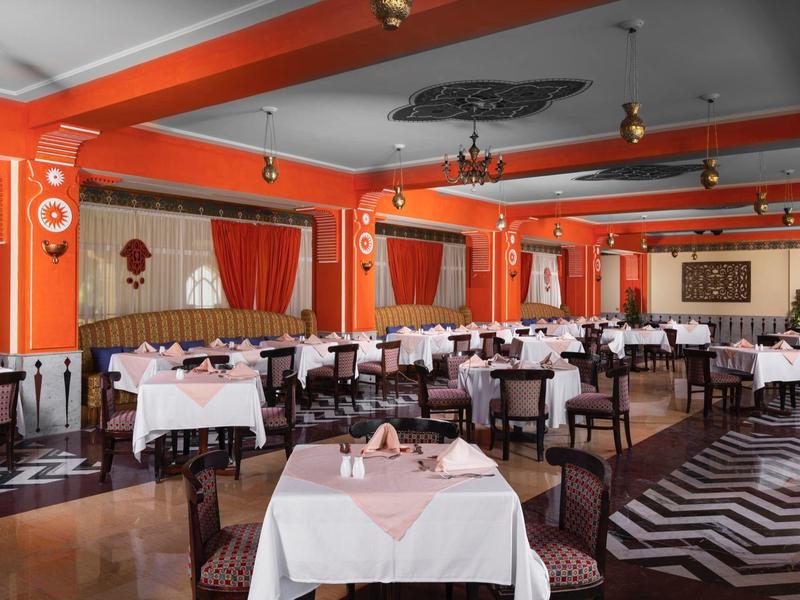 Large restaurant with orange walls, white tablecloths, and geometric floor pattern.