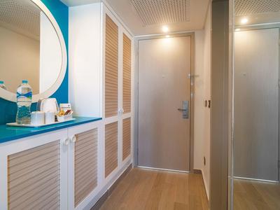 Korytarz z drewnianą podłogą, niebieską ścianą i szafką z butelkami wody i szklankami.