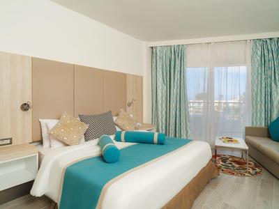 Nowoczesny pokój hotelowy z dużym łóżkiem, sofą i balkonem z zasłonami.