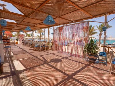 Zastřešená terasa s židlemi a stoly, výhled na pláž a moře u hotelu.