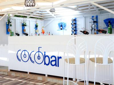 Moderní bílý vnitřní bar s modrým osvětlením a stylovými bílými židlemi.