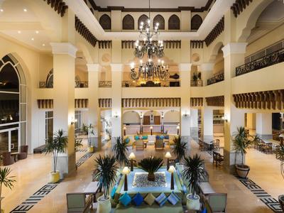 Duża lobby hotelowa z wysokimi kolumnami, żyrandolami i miejscami do siedzenia.