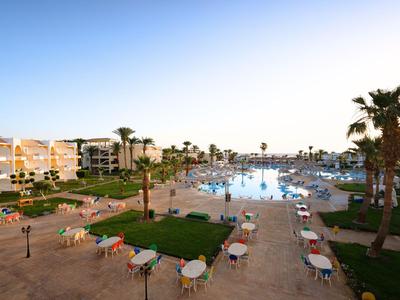 Hotelový areál s velkým bazénem, lehátky a palmami pod jasnou oblohou.