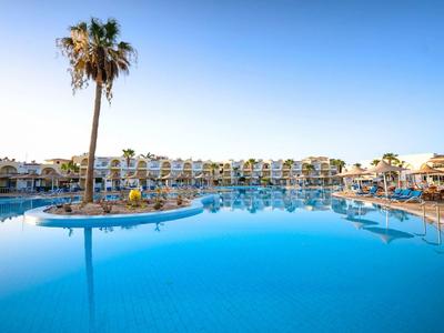 Grande piscina d'hotel con isola di palme e lettini sotto un cielo limpido.