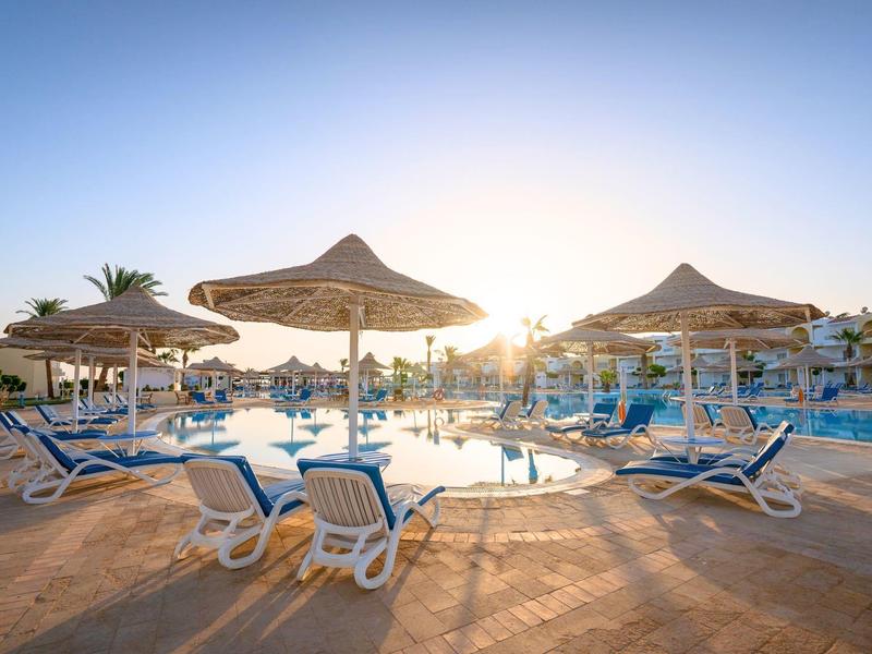 Zachód słońca przy basenie z leżakami i parasolami w ośrodku hotelowym.