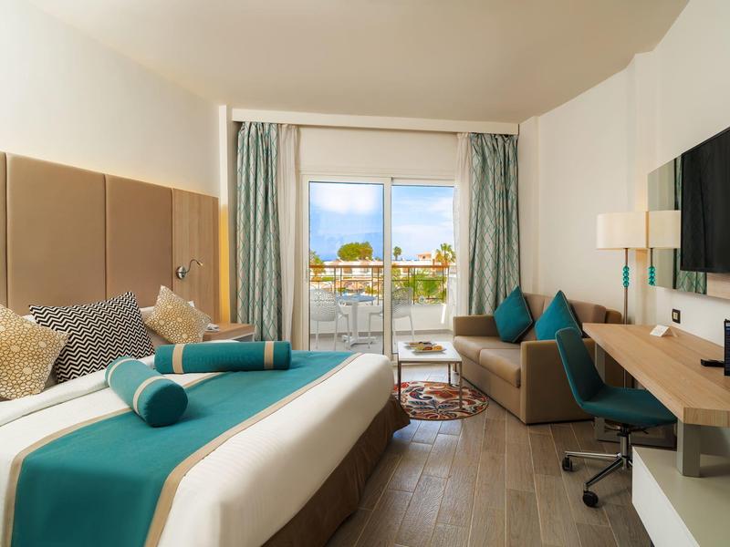 Nowoczesny pokój hotelowy z łóżkiem podwójnym, biurkiem i balkonem z miejscem do siedzenia.