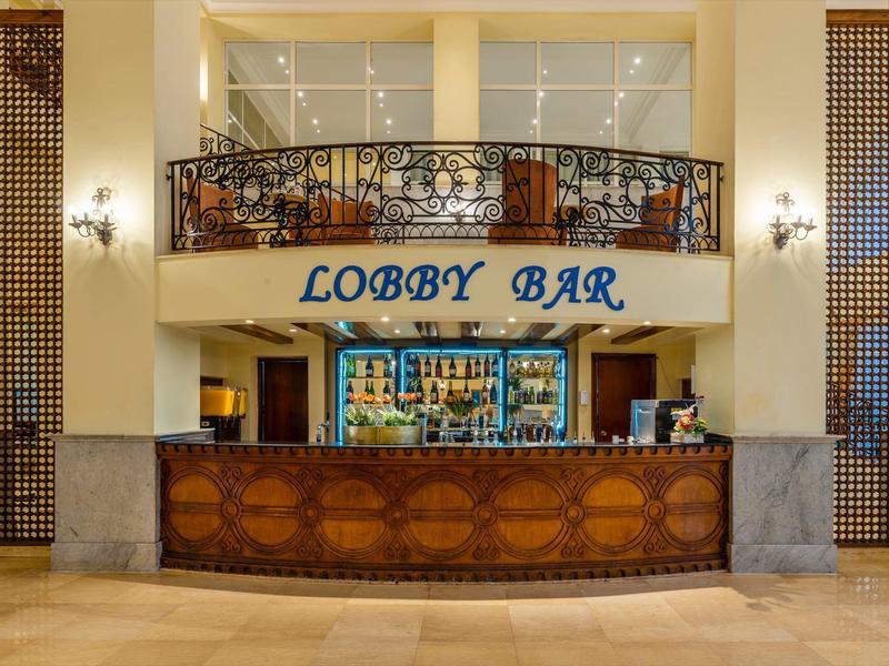 Eleganckie lobby hotelowe z ozdobnym drewnianym barem i napisem 'Lobby Bar'.
