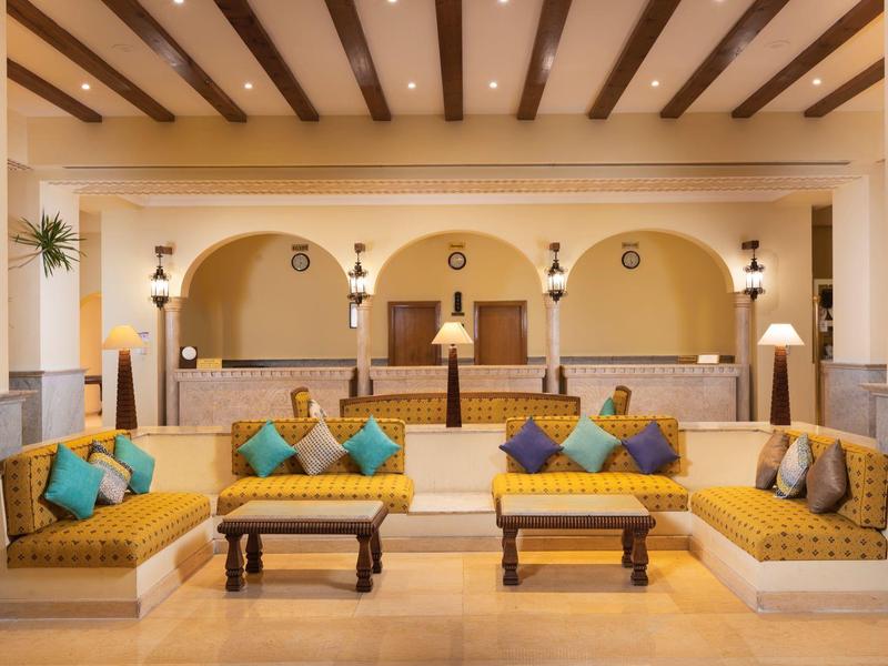 Nowoczesne lobby hotelowe z żółtymi sofami, poduszkami i kamiennymi kolumnami pod drewnianym sufitem z belkami.