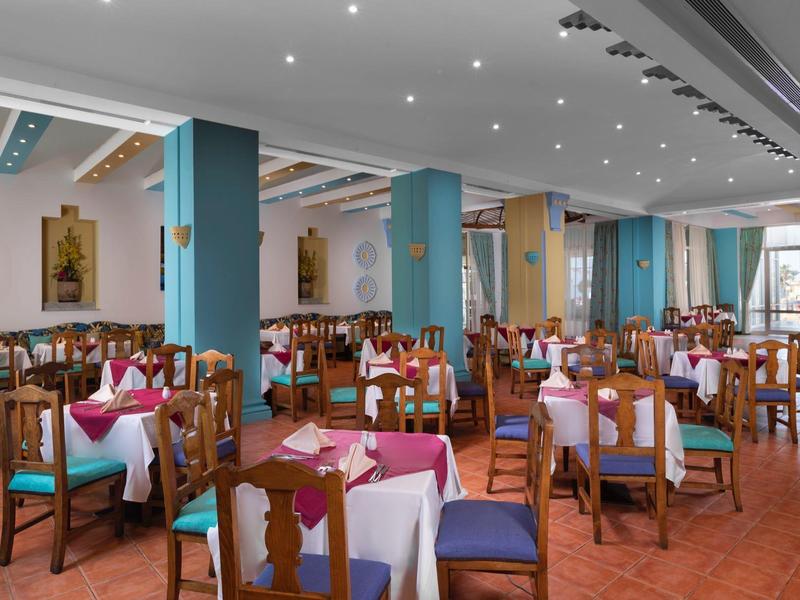 Restauracja z kolorowymi krzesłami, nakrytymi stołami i jasnym oświetleniem.