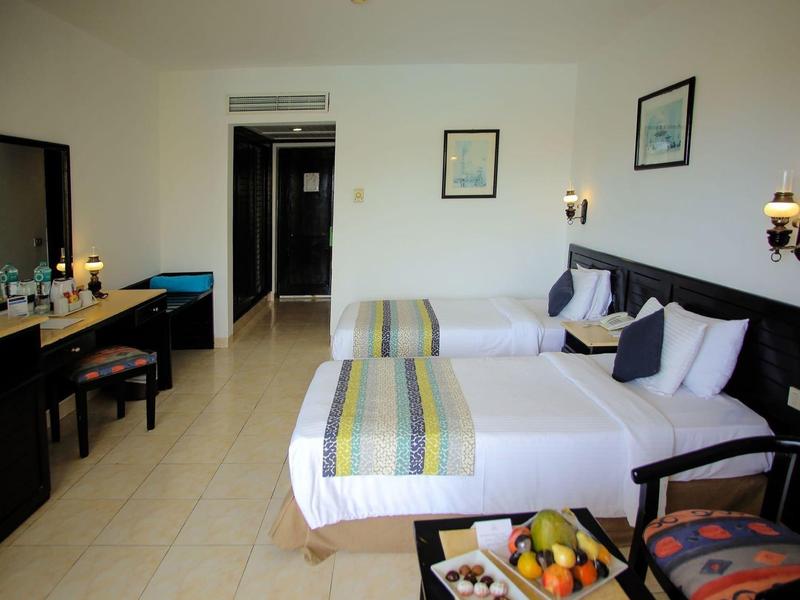 Pokój hotelowy z dwoma pojedynczymi łóżkami, biurkiem, krzesłem i koszem owoców na małym stoliku.