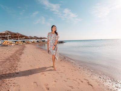 Frau läuft barfuß am Strand entlang, leicht bewölkter Himmel, sanfte Wellen am Ufer.