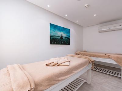 Zwei Behandlungsbänke mit beigen Decken in einem hellen Raum, an der Wand ein Bild und Klimaanlage.