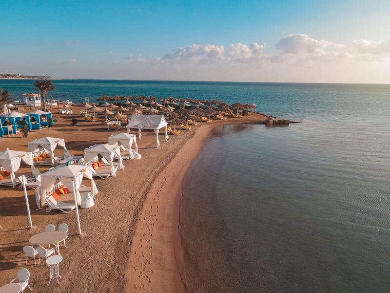 Piaszczysta plaża z białymi leżakami i widokiem na spokojne morze pod jasnym niebem.