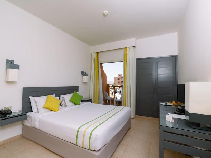 Jasny pokój hotelowy z podwójnym łóżkiem, małymi stolikami nocnymi i szafą.