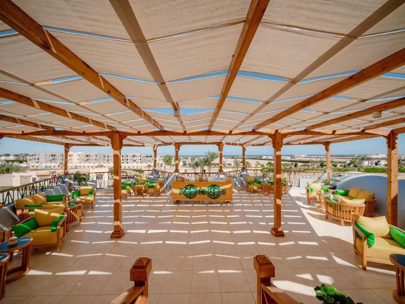 Zadaszony taras z zielonymi poduszkami i widokiem na morze.