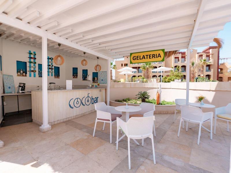 Zewnętrzny obszar gelaterii z białymi stołami i krzesłami pod zadaszonym patio.