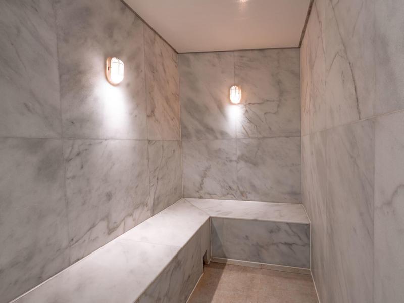 Wnętrze sauny z białymi marmurowymi ścianami i dwiema lampami ściennymi.