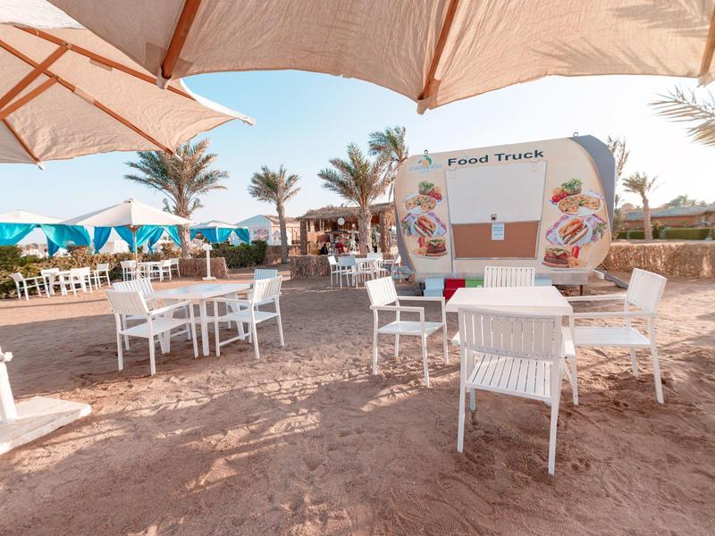 Miejsce do siedzenia z białymi krzesłami i stołami na piasku pod parasolami w hotelu nad morzem.