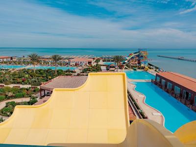 View from water slide over pool, garden, and sea in tropical resort under clear sky.