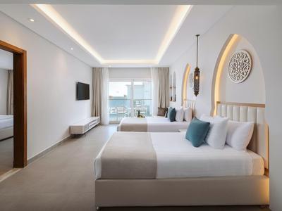 Bright hotel room with two beds, modern furniture, and sea view through glass windows.