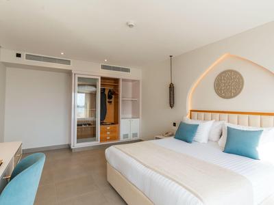 Bright hotel room with double bed, blue accent pillows, and modern desk chair.