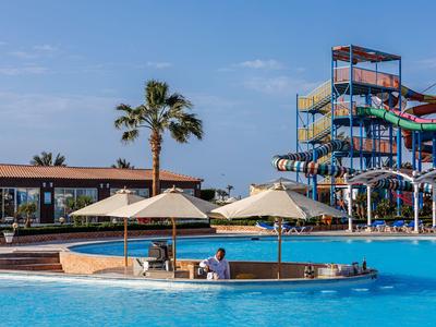 Groot hotelzwembad met parasols, ligstoelen en glijbanen op de achtergrond.