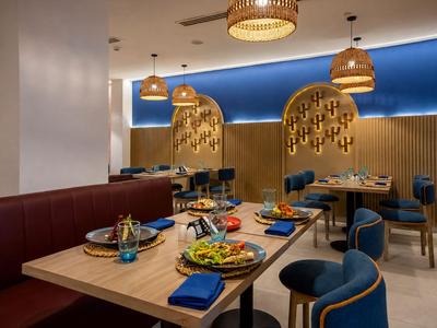 Moderne hotel eetgedeelte met stijlvolle tafels, blauw-gouden stoelen en decoratieve wandverlichting.