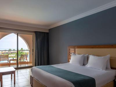 Hotel room with large bed, sea view, and balcony with table and chairs.