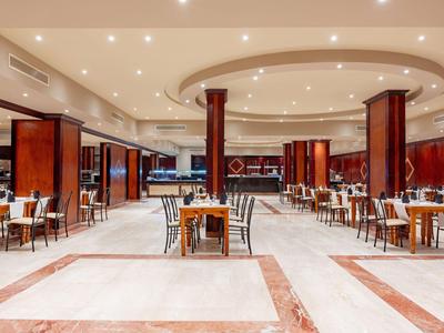 Duża sala jadalna z wieloma stołami i krzesłami, ciepło oświetlona i elegancko zaprojektowana.