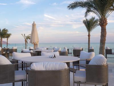 Terrace area with seating and sea view at sunset, palm trees line the space.