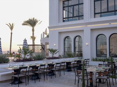 Modern hotel outdoor area with tables, chairs, and palm trees at sunset.