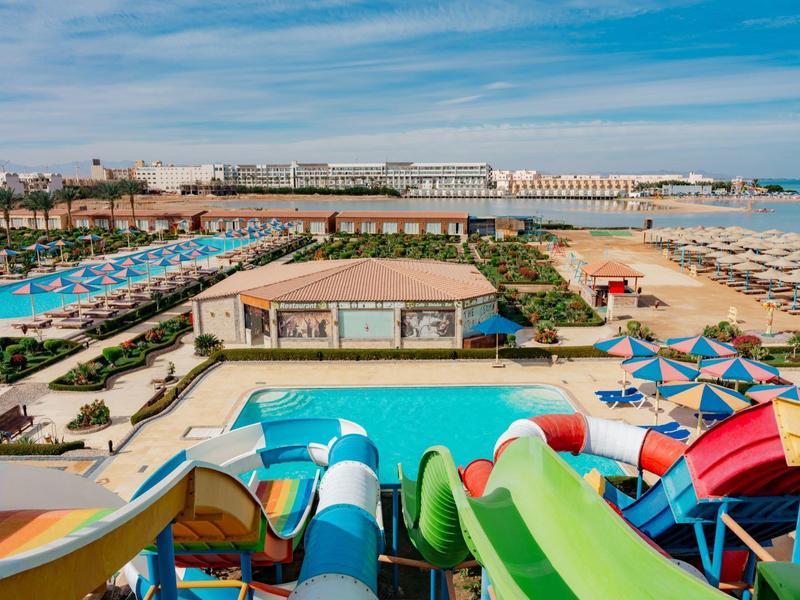 Widok na park wodny z kolorowymi zjeżdżalniami, basenem i plażą w tle.