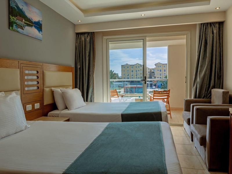 Pokój hotelowy z dwoma łóżkami, krzesłami, szafą i widokiem na basen i budynki