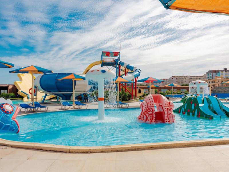 Piscine pour enfants avec toboggans colorés et jeux d'eau sous un ciel bleu.