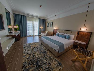 Modern hotel room with large bed, desk, chairs, and balcony with curtains.