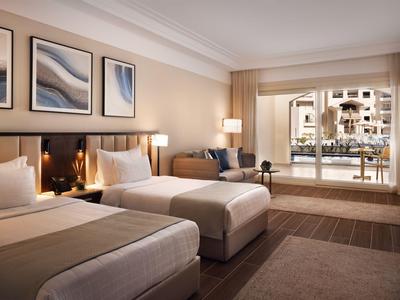Hotel room with two beds, sofa, and pool view through large windows.