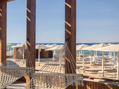 A hammock under a wooden pergola overlooking a beach with umbrellas.
