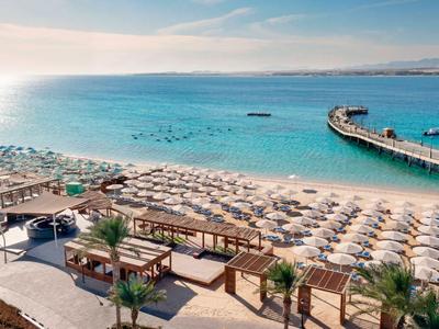 Beach hotel with numerous sun umbrellas and a long pier extending into the sea in clear weather.