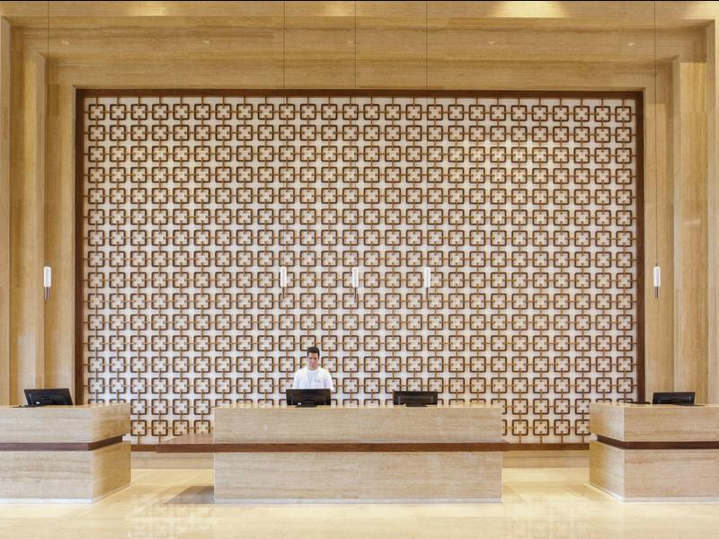 Modern wooden hotel reception area with geometric wall pattern and front desks.