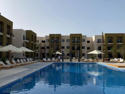 Großer Außenpool vor einem modernen Hotel mit Liegestühlen und Sonnenschirmen.