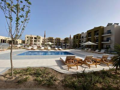 Moderner Hotelkomplex mit Außenpool, Liegestühlen und Sonnenschirmen unter klarem Himmel.