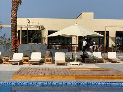 Piscina exterior moderna con tumbonas y sombrilla frente a un edificio de hotel bajo cielos despejados.