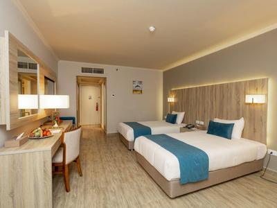 Chambre d'hôtel lumineuse avec deux lits simples, bureau et chaise, éclairage moderne et sol en bois.