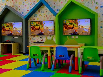 Espace de jeux coloré pour enfants avec petites tables, chaises et téléviseurs dans des niches en forme de maison.
