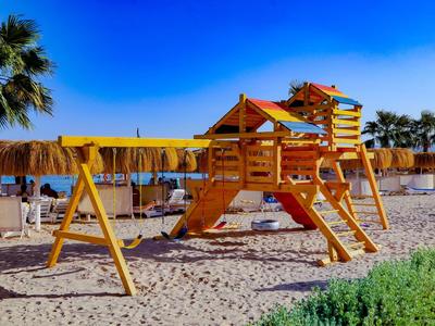 Aire de jeux en bois avec balançoire et structure d'escalade sur une plage de sable sous un ciel bleu