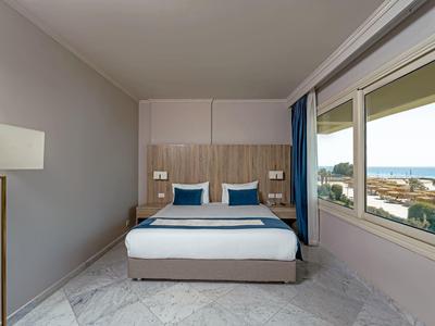 Chambre d'hôtel moderne avec lit double, lampes de chevet et vue sur la mer par une grande fenêtre.