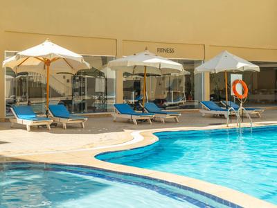 Poolbereich mit blauen Liegestühlen und weißen Sonnenschirmen vor gelber Hotelwand.