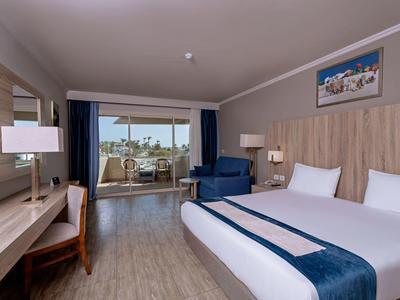 Chambre d'hôtel moderne avec lit double, bureau, fauteuil et balcon avec vue sur la mer.