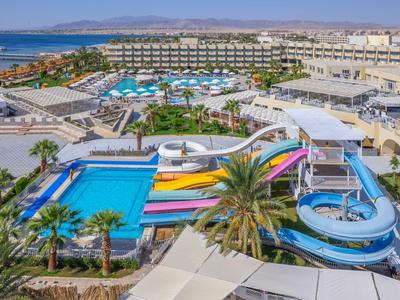 Vue d'un hôtel avec toboggans aquatiques, piscines et la mer en arrière-plan.