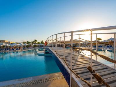 Ein breiter Pool mit einer geschwungenen Brücke und Liegestühlen bei Sonnenuntergang.